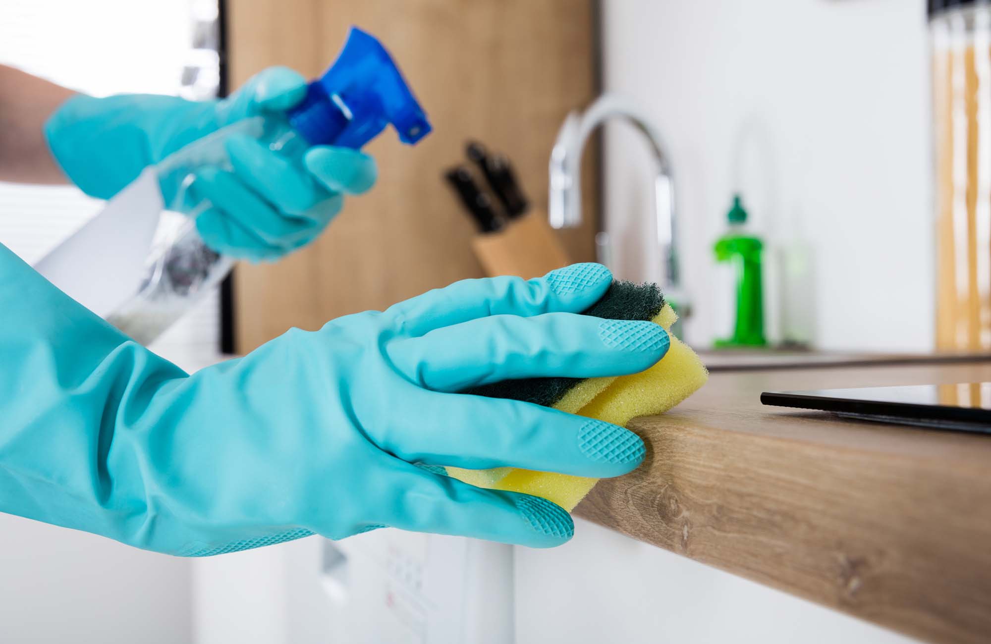 Janitor Cleaning Kitchen Worktop With Sponge And Spray Bottle